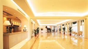 Un vestíbulo de hotel con mostrador de recepción, plantas en macetas y un suelo pulido.