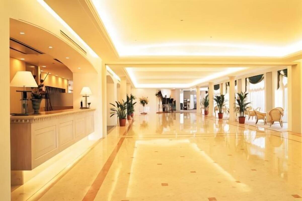 A hotel lobby with a reception desk, potted plants, and a polished floor.
