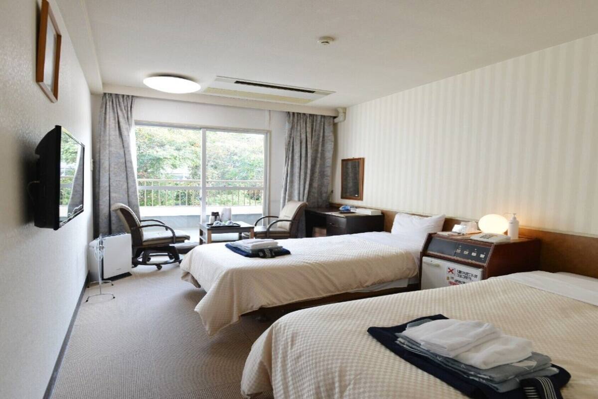 A hotel room with two beds, a desk, a chair, a TV, and a window with curtains.