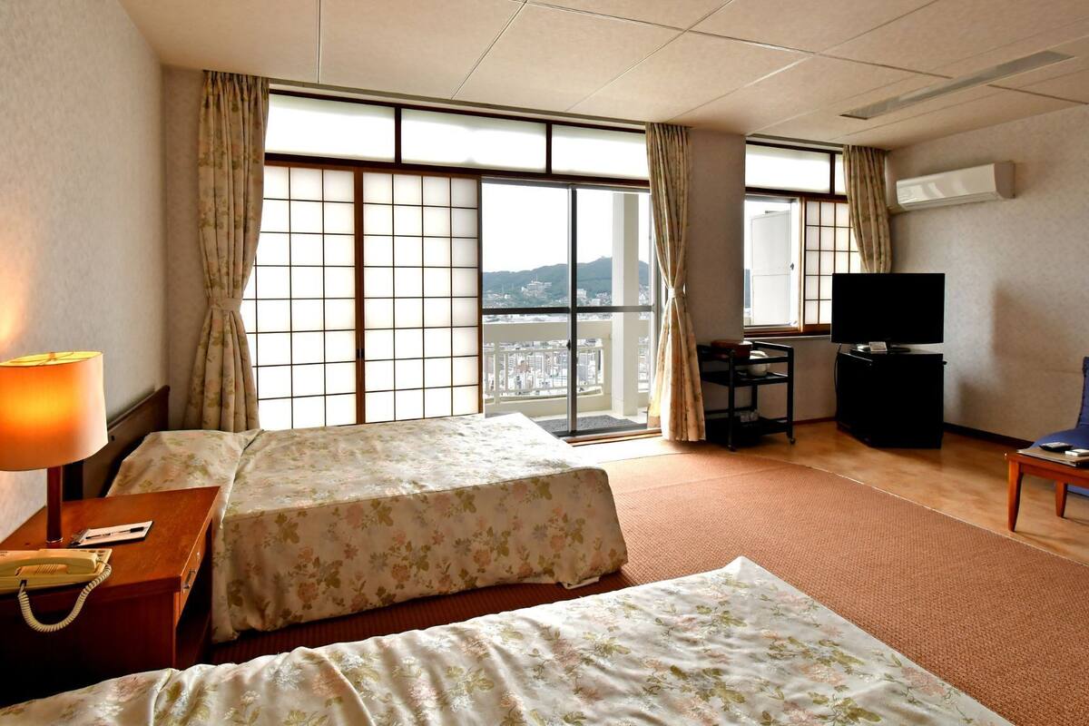 A hotel room with two beds, a desk with a telephone, a television, and a sofa.