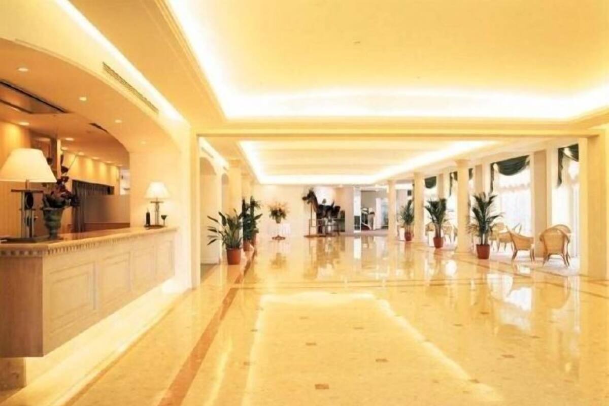 A spacious hotel lobby with a polished floor, a reception desk, and potted plants.