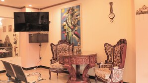 A dining area with ornate chairs, a round table, a flat-screen TV, and a large painting on the wall. - Hotel Plaza Garibaldi (Caldas)