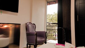 A hotel room with a bed, a chair, a TV, and a balcony with a view of trees. - Hotel Plaza Garibaldi (Caldas)