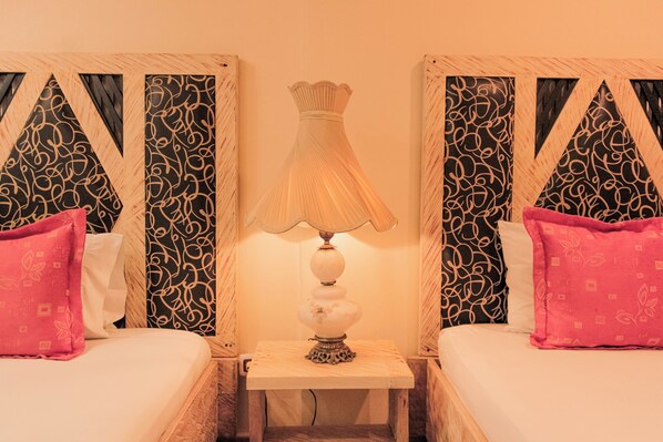 Habitación de hotel con dos camas, una mesita de noche con lámpara y papel tapiz estampado.