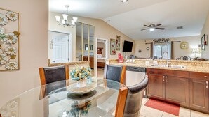 A modern kitchen with a glass dining table, wooden chairs, a built-in oven, and a large mirror above the sink.