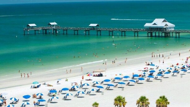 A beach with a pier extending into the ocean, featuring several beach umbrellas and lounge chairs.