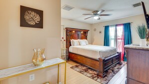A bedroom with a wooden bed, a marble bedside table, a ceiling fan, and a large window with curtains.