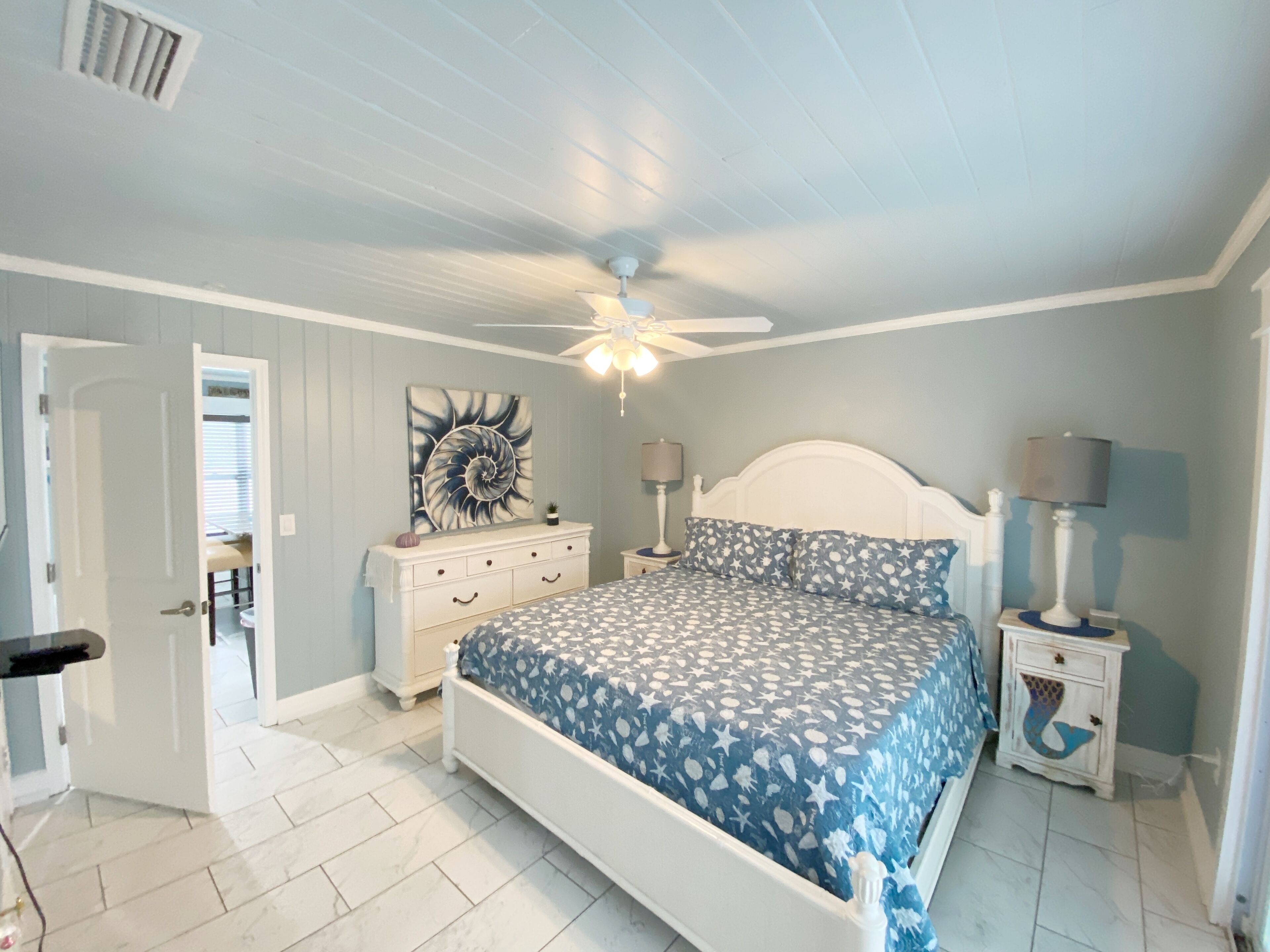 A bedroom with a bed, a ceiling fan, a nightstand, a dresser, and a wall art piece.