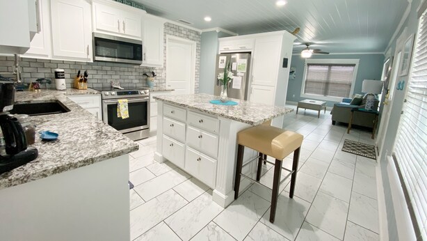 Una cocina moderna con armarios blancos, encimera de granito y una isla central con banco.