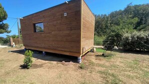 A small wooden cabin with a window, situated in a grassy area with trees in the background.