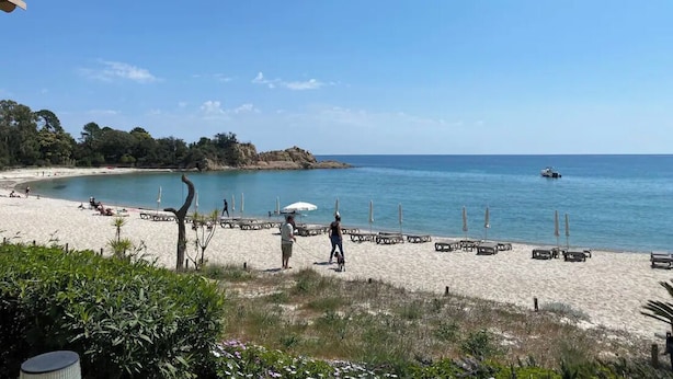 A beach with a clear sky, a sandy shore, and a few people walking.