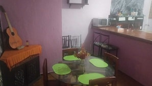 A dining area with a glass table, green placemats, a guitar, and a microwave on the counter.