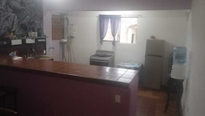 A compact kitchen with a tiled countertop, a stove, a refrigerator, and a water dispenser.