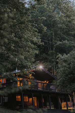 A wooden cabin with a deck, surrounded by dense trees.