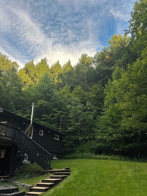A rustic cabin with a chimney, surrounded by lush greenery and a clear sky.