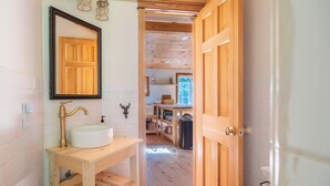 A wooden interior with a sink, mirror, and open door leading to a kitchen area.