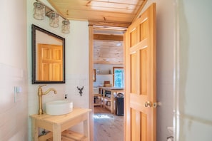Un intérieur en bois avec un évier, un miroir et une porte ouverte donnant sur un espace cuisine.