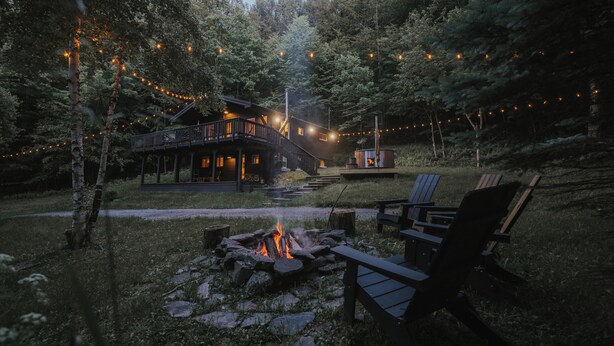 A cabin with a deck, a fire pit, and string lights.