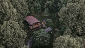 An aerial view of a cabin with a deck, hot tub, and fire pit surrounded by dense forest.