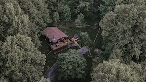 An aerial view of a cabin with a deck, hot tub, and fire pit surrounded by dense forest.