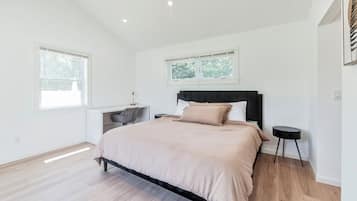 Ein Schlafzimmer mit Bett, Schreibtisch und Stuhl. Zwei Fenster und eine Deckenleuchte sind vorhanden.
