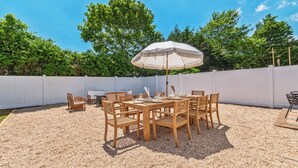 Un patio de madera con una mesa, sillas, una sombrilla y una valla blanca.