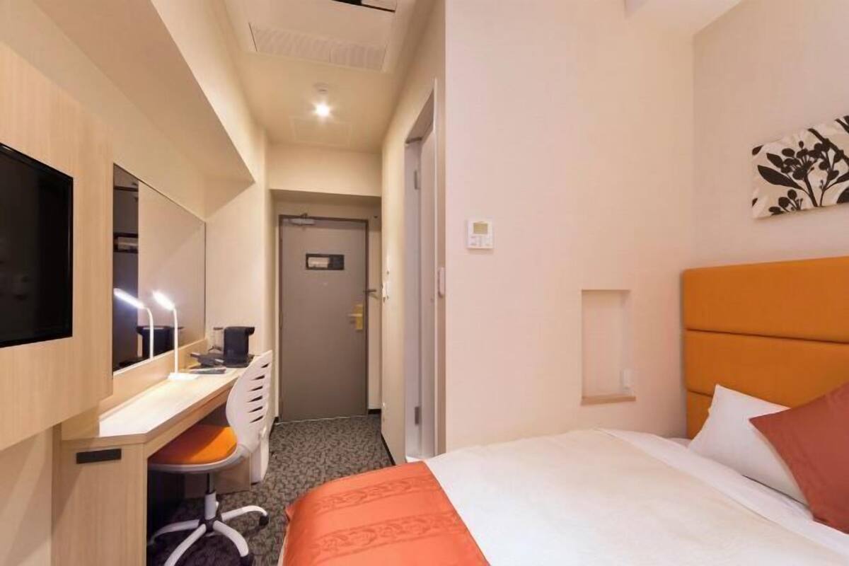 A hotel room with a bed, a desk with a chair, a television, and a door leading to another room.