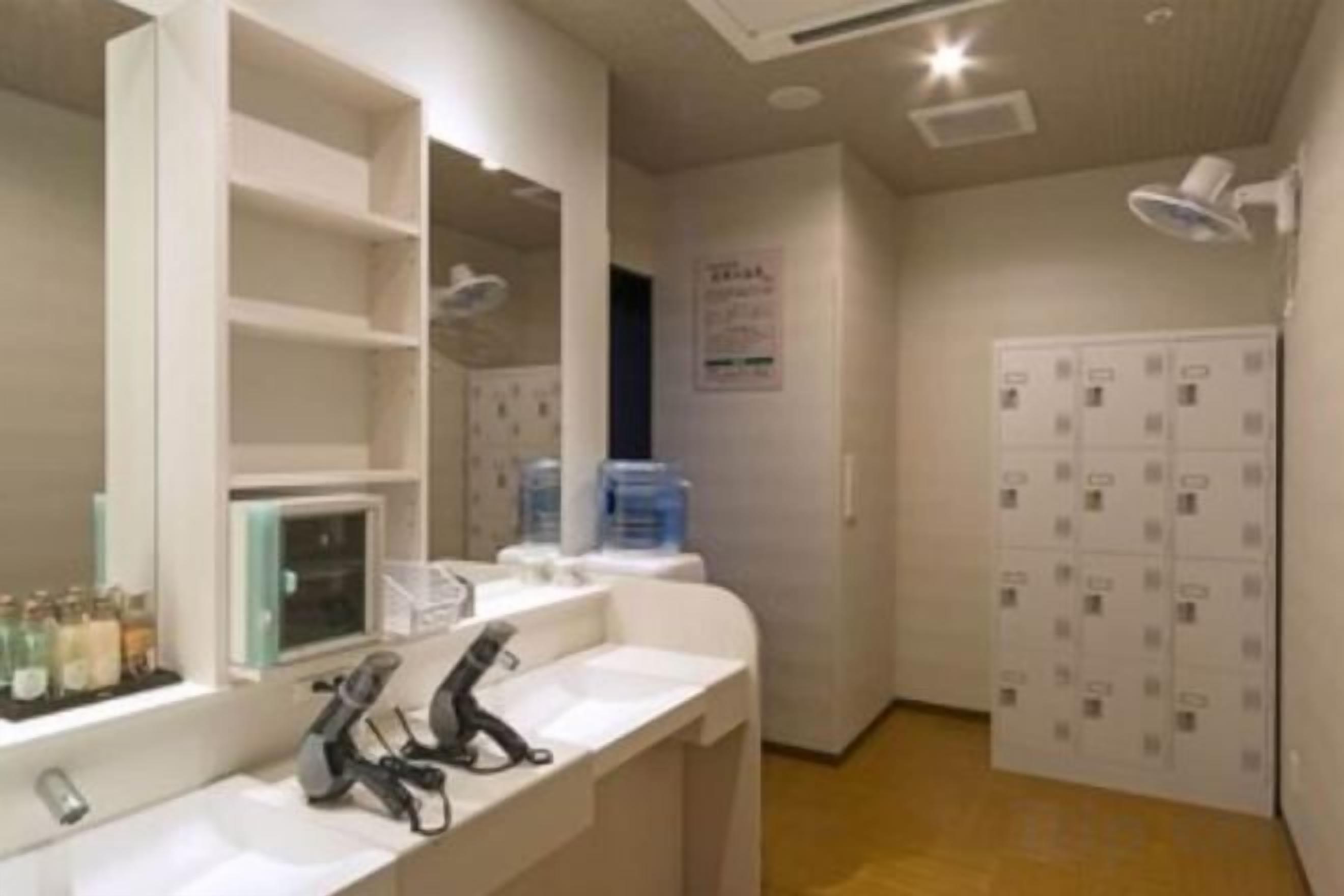 A hotel bathroom with a large mirror, a sink, and a shower area. There are shelves with toiletries and a sign on the wall.