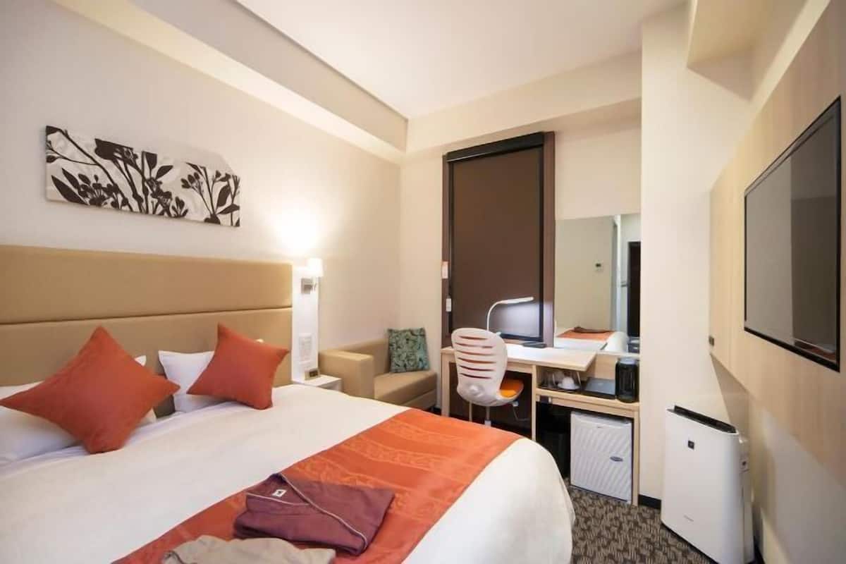 A hotel room with a bed, desk, chair, and a television.