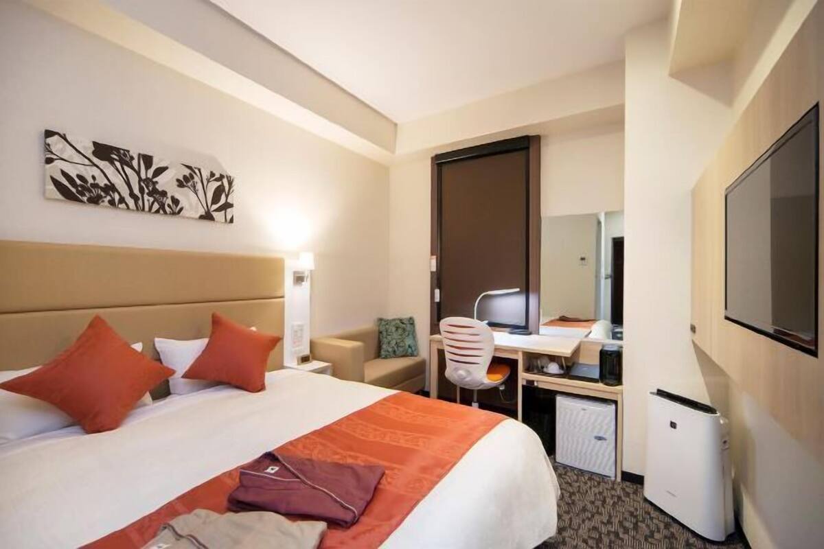 A hotel room with a bed, a desk, a chair, a television, and a wardrobe.