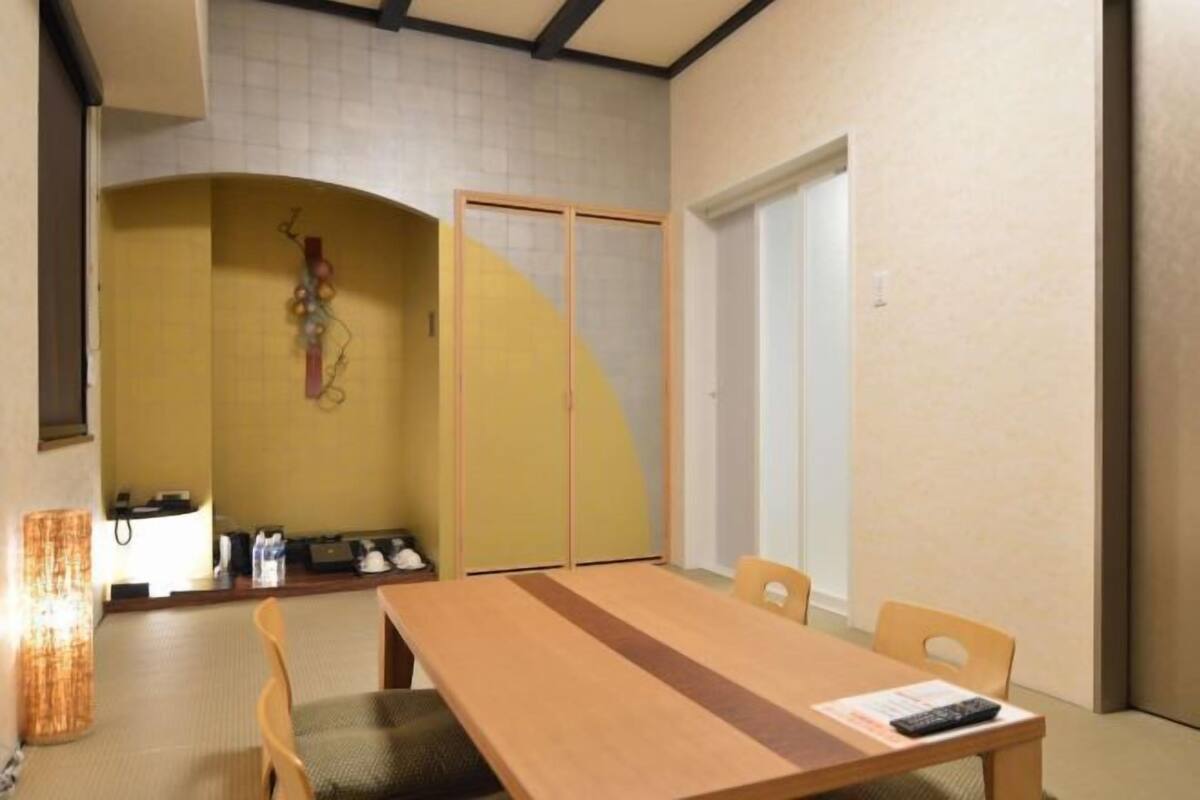 A hotel room with a wooden dining table, chairs, a small kitchen area, and a sliding door closet.