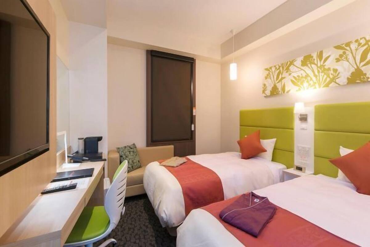 A hotel room with two beds, a desk, a chair, a television, and a wall-mounted artwork.
