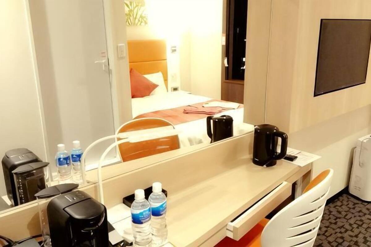 A hotel room with a bed, a coffee maker, a mirror, a desk with a chair, and a water bottle.