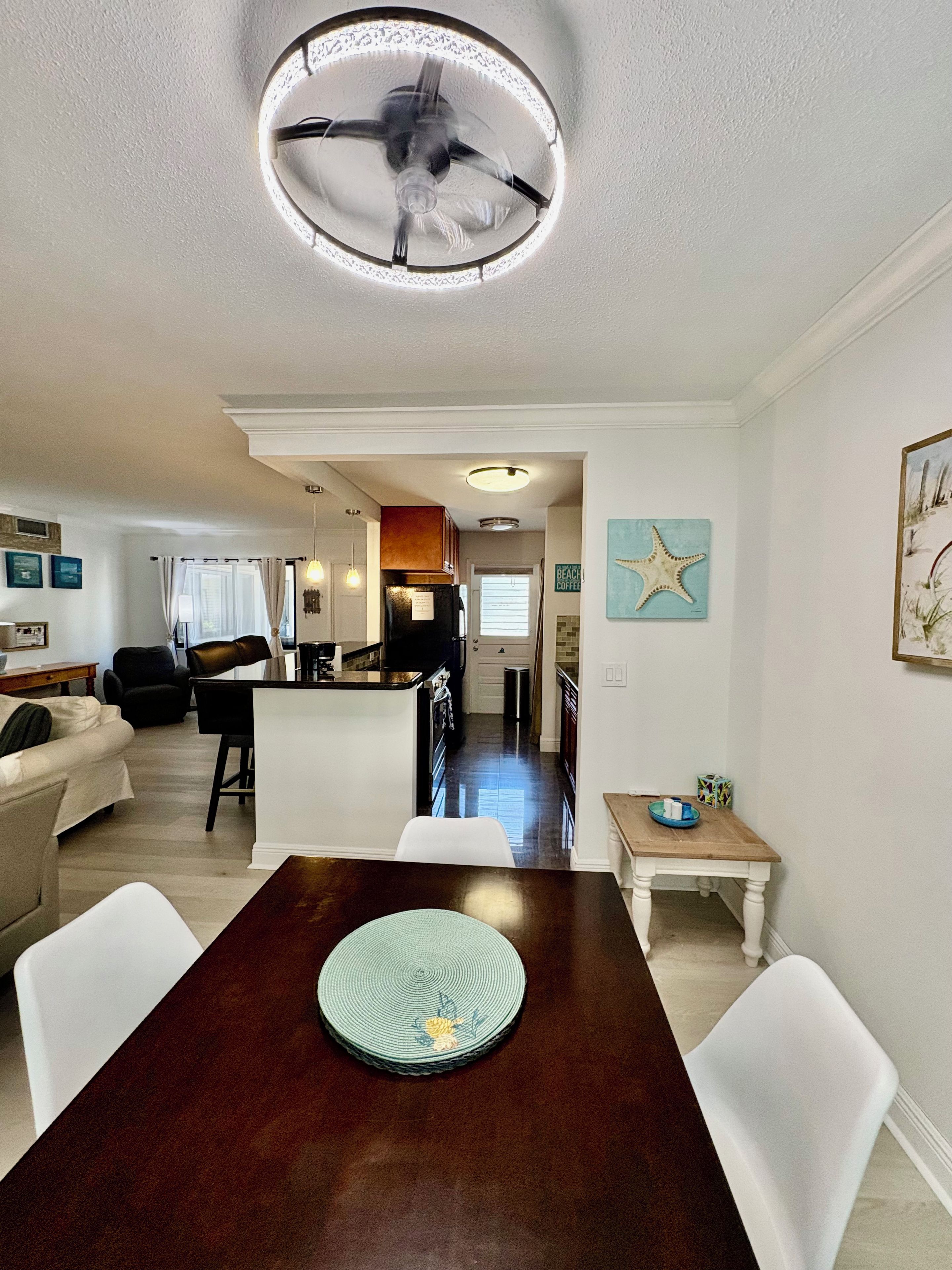 A dining area with a wooden table, white chairs, and a ceiling fan.