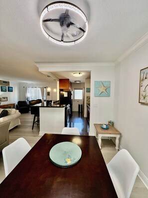 A dining area with a wooden table, white chairs, and a ceiling fan.