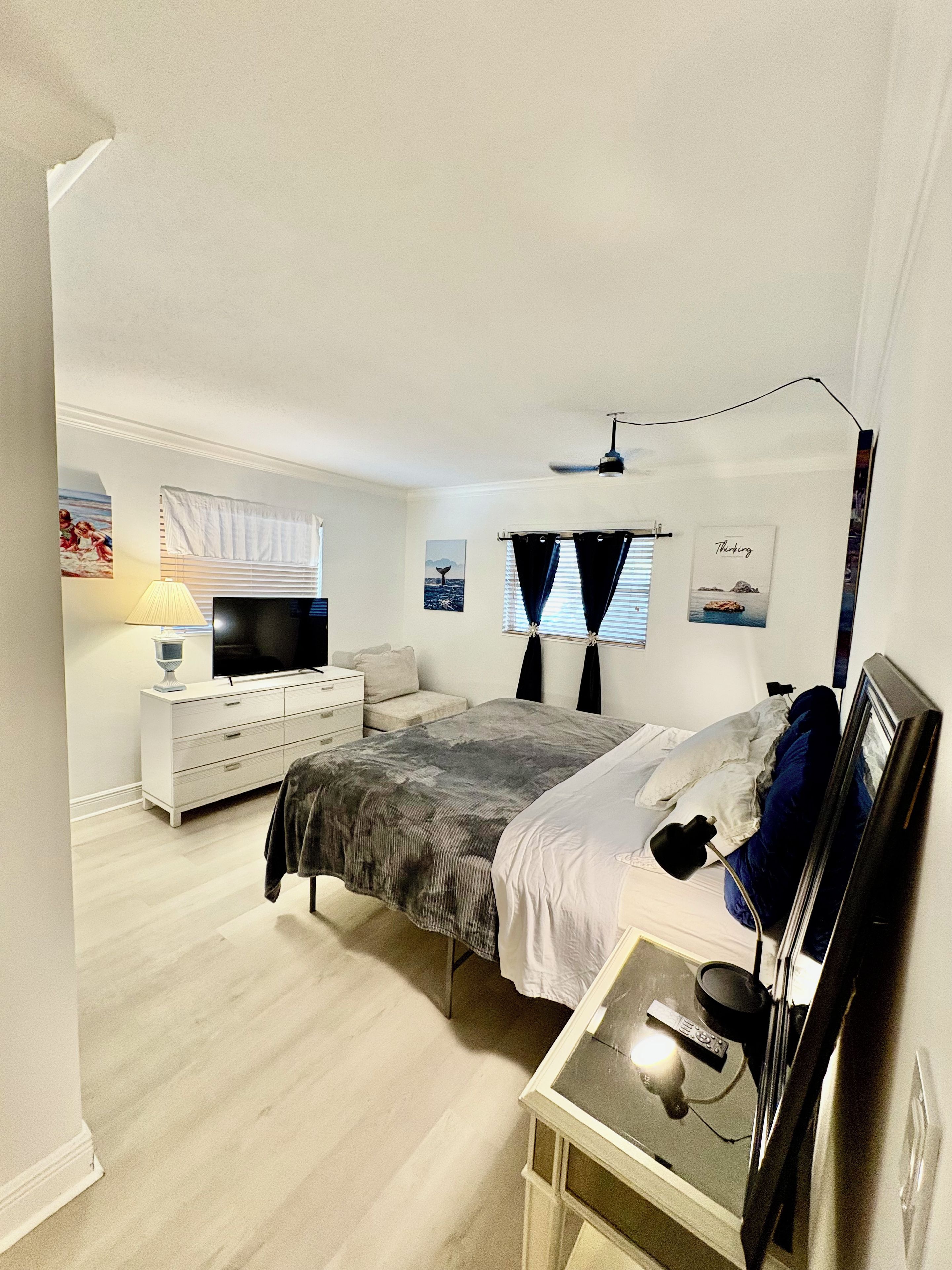 A bedroom with a bed, bedside table, lamp, TV, and a window with curtains.