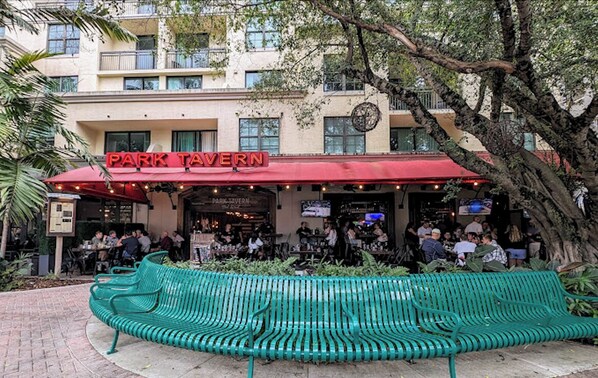 A park tavern with outdoor seating and a green bench in the foreground.