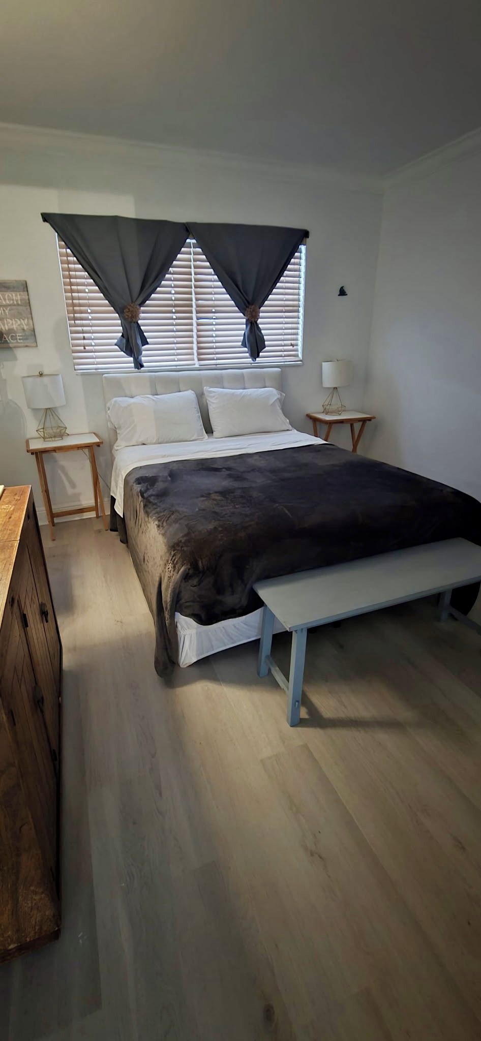 A bedroom with a bed, bedside tables, a bench, a window with curtains, and a wooden dresser.
