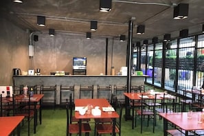 A restaurant with tables and chairs, a bar counter, and large windows. - My Loft Hotel (Chiang Mai)