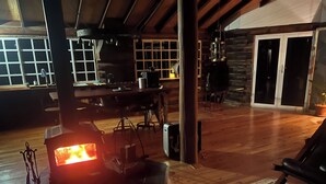 A cozy living room with a fireplace, wooden flooring, and a large window. - Log Cabin OFF GRID, fire place, balconies/library/ Rain forrest, walk, swim.  (Elands)