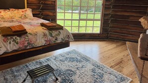 A log cabin bedroom with a large bed, a window with a view of the outdoors, a chandelier, and a hanging chair. - Log Cabin OFF GRID, fire place, balconies/library/ Rain forrest, walk, swim.  (Elands)