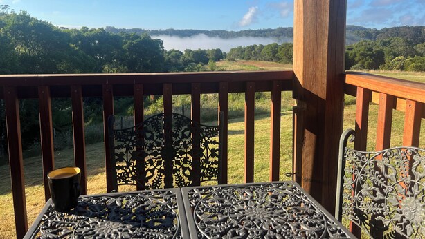 A wooden balcony with a metal railing and a table with a cup. - Log Cabin OFF GRID, fire place, balconies/library/ Rain forrest, walk, swim.  (Elands)