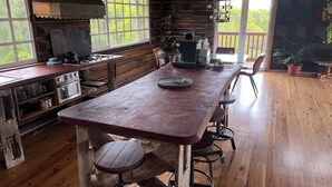 A rustic kitchen with wooden countertops, a large island with stools, and a view of greenery outside. - Log Cabin OFF GRID, fire place, balconies/library/ Rain forrest, walk, swim.  (Elands)