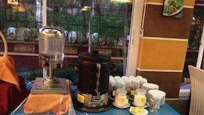 A table with a coffee machine, cups, and condiments.
