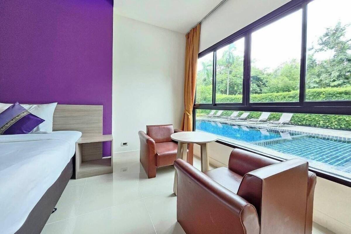 Habitación de hotel con cama, una mesita, dos sillas y ventana con vista a una piscina.