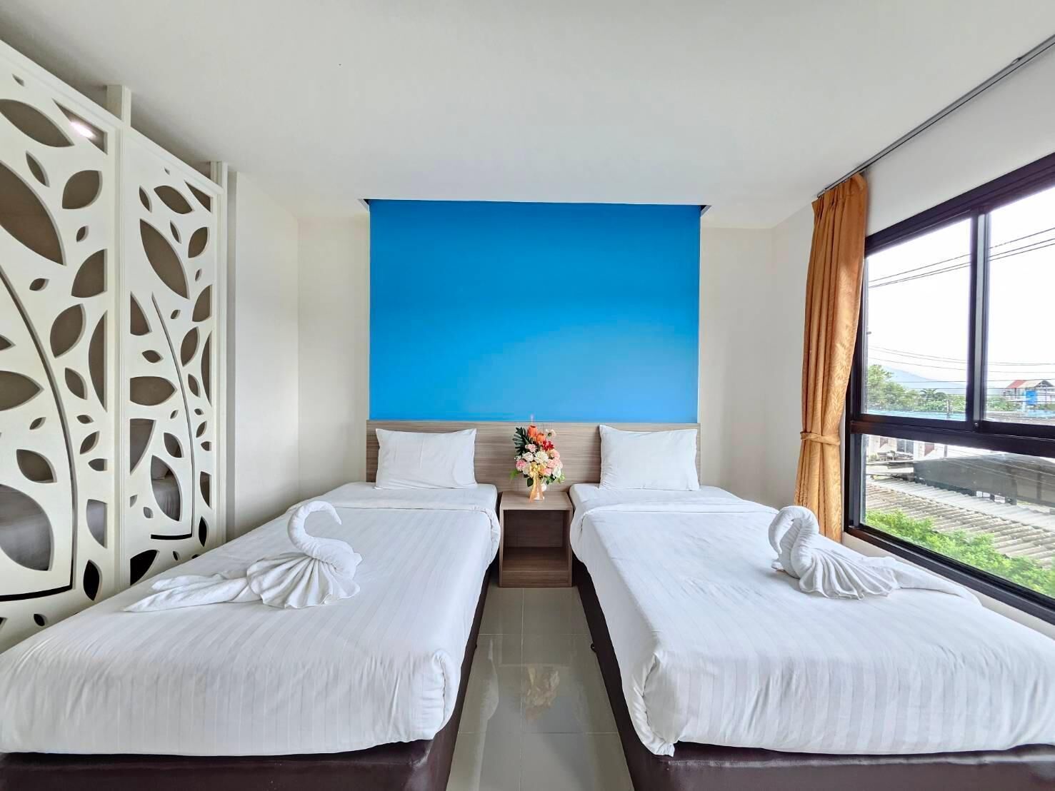 Habitación de hotel con dos camas, una pared de acento azul, un separador decorativo y vistas al exterior.