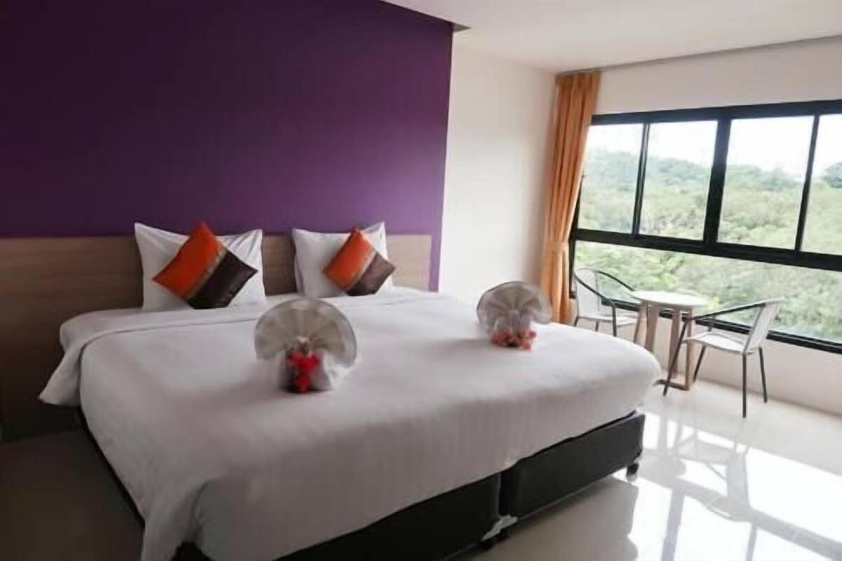 Habitación de hotel con una cama grande, vistas a zonas verdes por la ventana y una pequeña mesa con sillas.