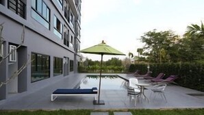 A modern building with a swimming pool, lounge chairs, and a green umbrella.