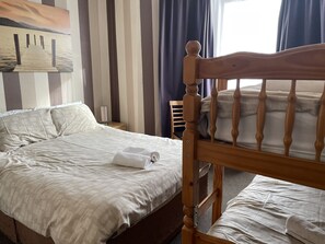 Una cama bien hecha con cabecera de madera, una mesita de noche con lámpara, y una pared a rayas con un cuadro.