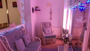 Una habitación acogedora con un sofá blanco, un sillón acolchado, una mesita con un florero y una alfombra azul estampada.
